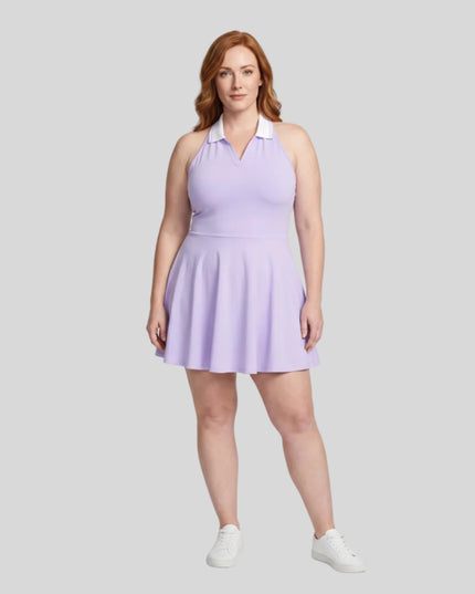 Woman modeling a purple TrackLine Court Dress, a halter-neck skater dress with a white collar, paired with white sneakers, against a light gray studio background.