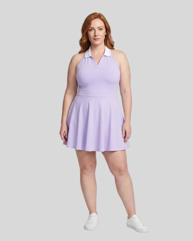 Woman modeling a purple TrackLine Court Dress, a halter-neck skater dress with a white collar, paired with white sneakers, against a light gray studio background.