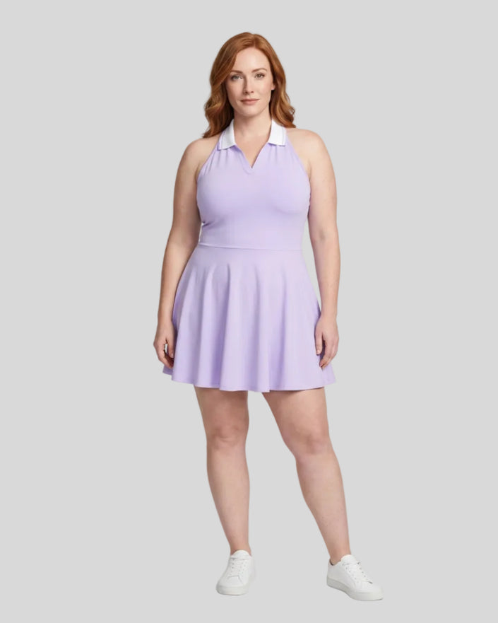 Woman modeling a purple TrackLine Court Dress, a halter-neck skater dress with a white collar, paired with white sneakers, against a light gray studio background.