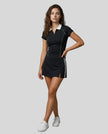 Female model wearing the TrackLine Court Polo in Black paired with Trackline Slit Skirt in Black, viewed full body from the front