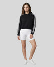 Full body front view of a woman wearing the Athlesi TrackLine Cropped Hoodie in black styled in a modern architectural setting