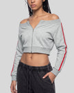 A woman wearing a flower gray off-the-shoulder cropped zip-up TrackLine Edge Jacket with red side stripes and dark gray sweatpants.