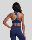 Model wearing the Athlesi TrackLine Edge Sports Bra in navy blue with white contrast trim and racerback design, back view