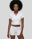 Upper body front view of a woman wearing the Athlesi TrackLine Lapel Crop Top in white