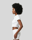 Side view of a woman wearing the Athlesi TrackLine Lapel Crop Top in white