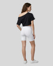 Full body back view of the Athlesi TrackLine Off-Shoulder Tee in black in a clean modern architectural environment