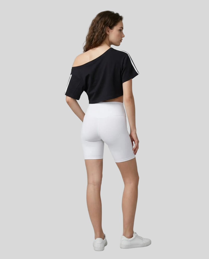 Full body back view of the Athlesi TrackLine Off-Shoulder Tee in black in a clean modern architectural environment
