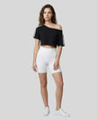 Full body front view of a woman wearing the Athlesi TrackLine Off-Shoulder Tee in black styled for modern athleisure movement