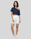 Full body front view of a woman wearing the Athlesi TrackLine Off-Shoulder Tee in blue styled for modern athleisure movement