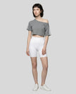 Full body front view of a woman wearing the Athlesi TrackLine Off-Shoulder Tee in gray styled for modern athleisure movement