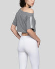Back angled view of the Athlesi TrackLine Off-Shoulder Tee in gray styled with elevated athleisure pieces