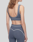 Back angled view of a model wearing the TrackLine Outline Sports Bra in Haze Blue