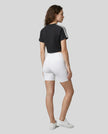Full body back view of the Athlesi TrackLine Performance Crop Tee in black in a clean architectural setting