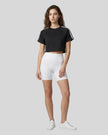 Full body front view of a woman wearing the Athlesi TrackLine Performance Crop Tee in black styled with modern athleisure pieces