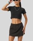 Mid body front view of the Athlesi TrackLine Performance Crop Tee in black styled in a modern minimalist setting