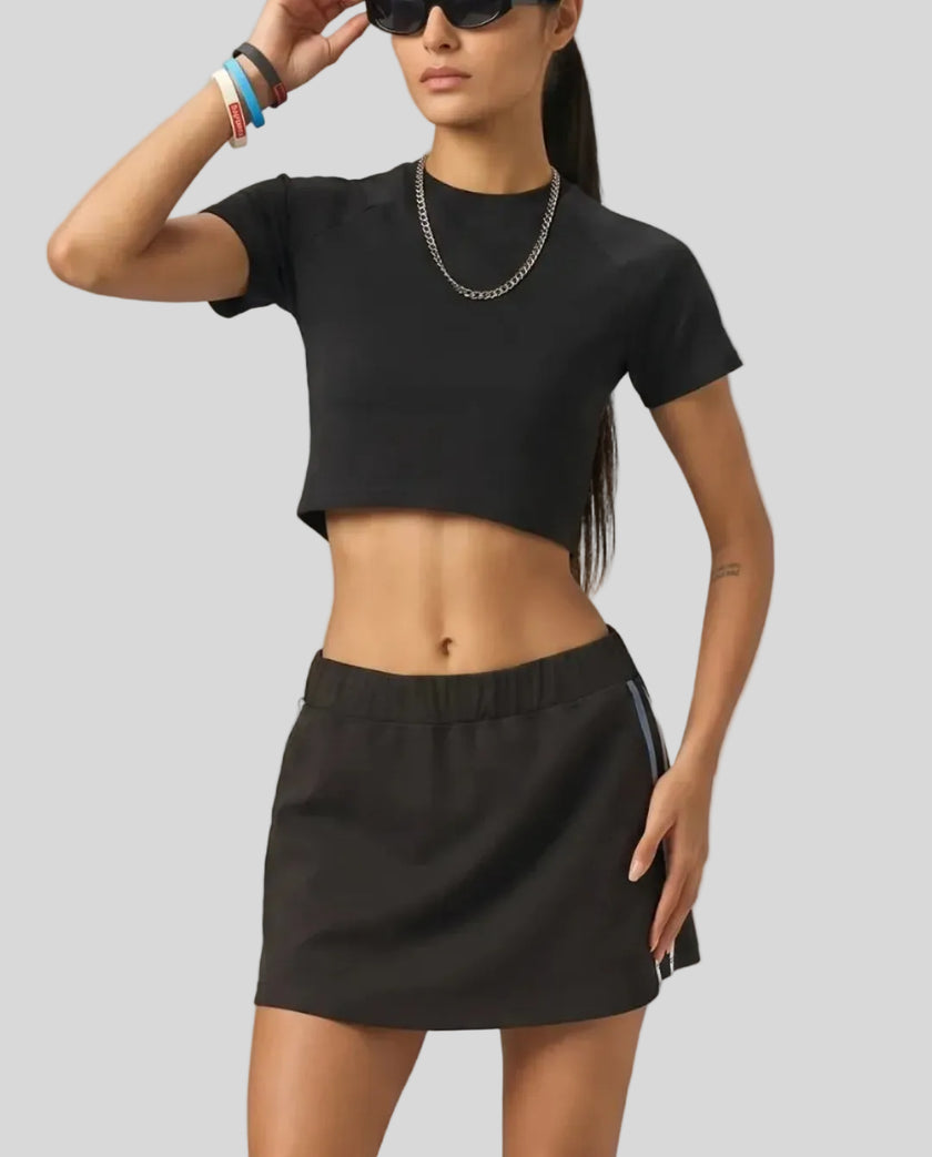 Mid body front view of the Athlesi TrackLine Performance Crop Tee in black styled in a modern minimalist setting