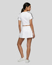 Full body back view of a woman wearing the Athlesi TrackLine Performance Crop Tee in white styled with Athlesi TrackLine Active Skort in white