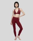 A woman modeling a matching wine red TrackLine Riviera activewear set consisting of a sports bra with white piping and high-waisted leggings with white side stripes, paired with white sneakers, against a plain white studio background.