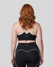 Upper body back view of woman wearing black TrackLine Sculpt Sports Bra with white crossover straps