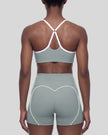 Mid body back view of woman wearing haze blue TrackLine Sculpt Sports Bra with white crossover straps