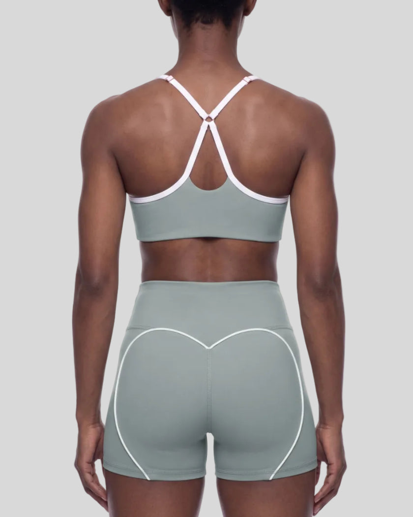 Mid body back view of woman wearing haze blue TrackLine Sculpt Sports Bra with white crossover straps