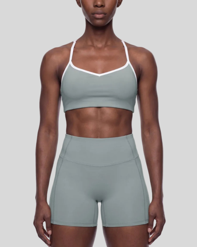 Mid body front view of woman wearing haze blue TrackLine Sculpt Sports Bra with white contrast trim