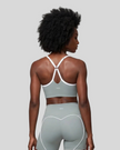 Upper body back view of woman wearing haze blue TrackLine Sculpt Sports Bra with white crossover straps