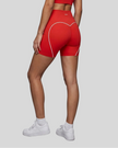 Lower body angled back view of woman wearing red TrackLine Sculpt Shorts highlighting curved white piping