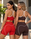  Back view of two models wearing red and brown TrackLine Sculpt Sports Bra with white contrast trim and matching short