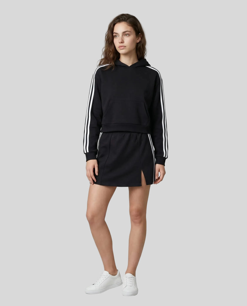 Full body front view of the Athlesi TrackLine Slit Skirt in black styled with the TrackLine Cropped Hoodie
