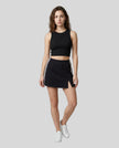 Full body front view of the Athlesi TrackLine Slit Skirt in black styled with a black cropped tank top