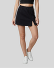 Lower body front view of a woman wearing the Athlesi TrackLine Slit Skirt in black