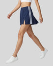 Lower body side walking view of a woman wearing the Athlesi TrackLine Slit Skirt in blue