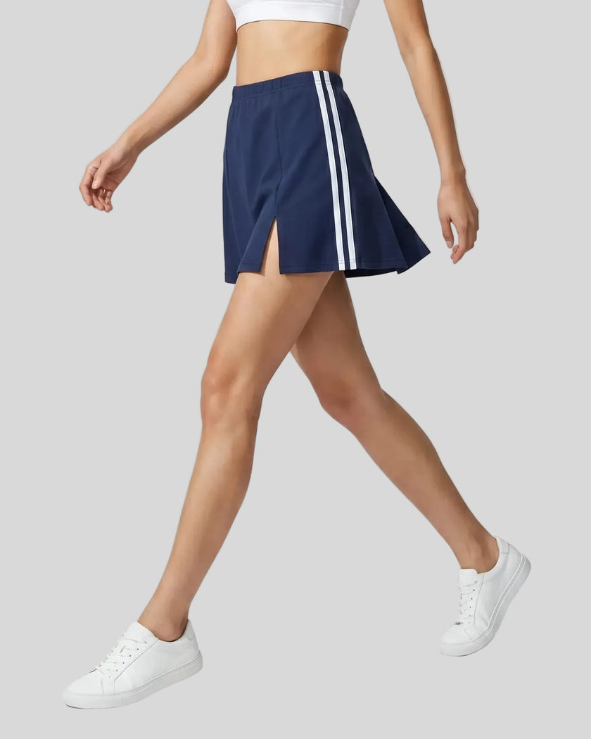 Lower body side walking view of a woman wearing the Athlesi TrackLine Slit Skirt in blue