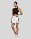 Full body front view of the Athlesi TrackLine Slit Skirt in white styled with a black cropped tank top