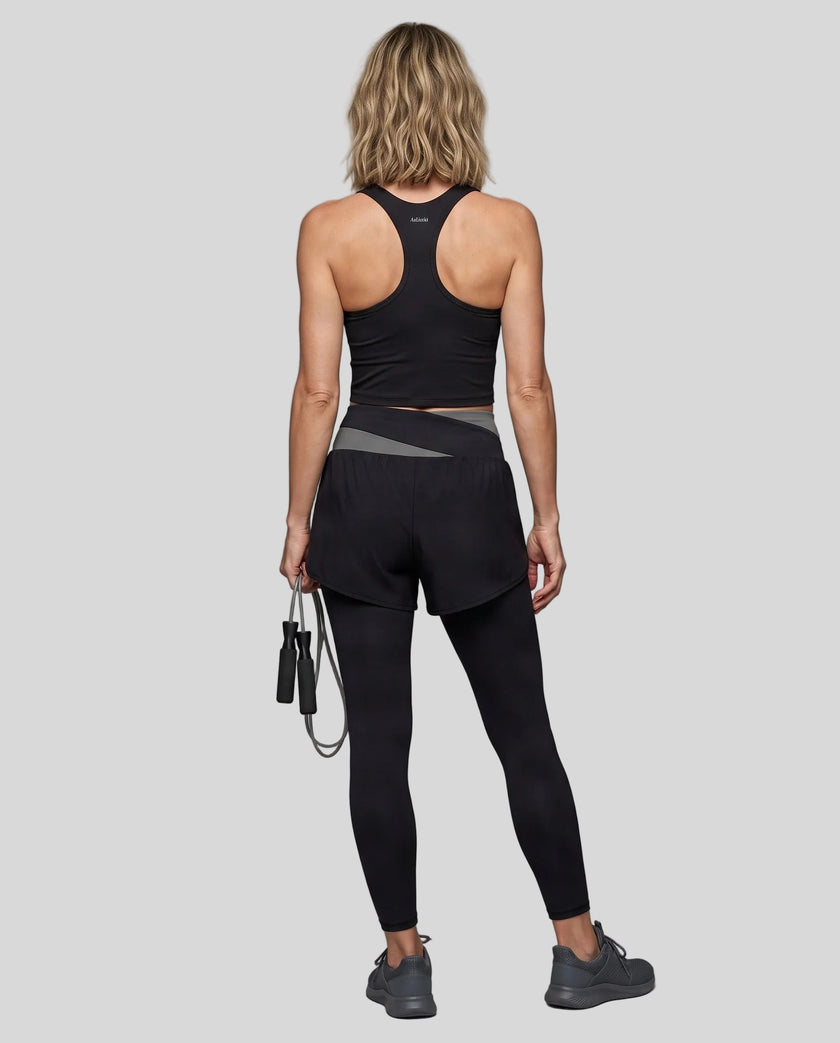 Full body back view of woman wearing TrackLine Synergy Layered Leggings in black and dark gray