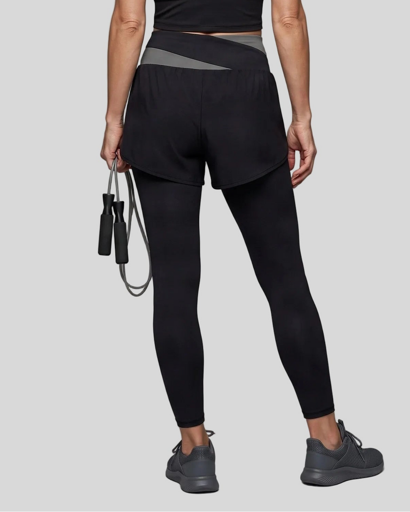 Lower body back view of woman wearing TrackLine Synergy Layered Leggings in black with dark gray crossover waistband