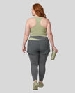 Full body back view of woman wearing TrackLine Synergy Layered Leggings in dark gray and bean green