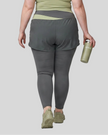 Lower body back view of woman wearing TrackLine Synergy Layered Leggings in dark gray with bean green crossover waistband