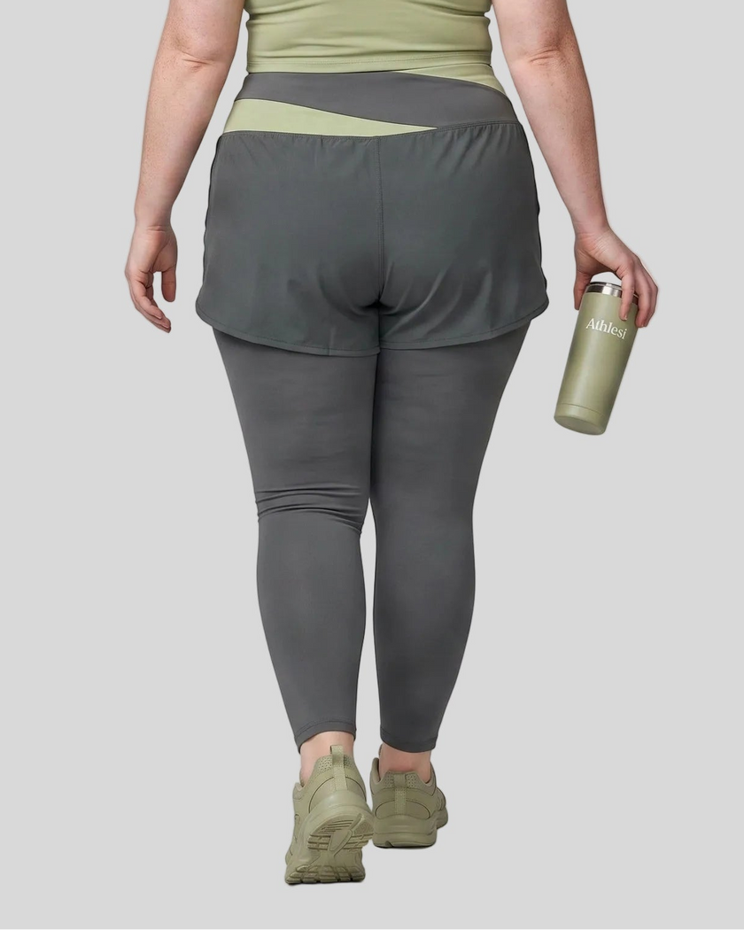Lower body back view of woman wearing TrackLine Synergy Layered Leggings in dark gray with bean green crossover waistband