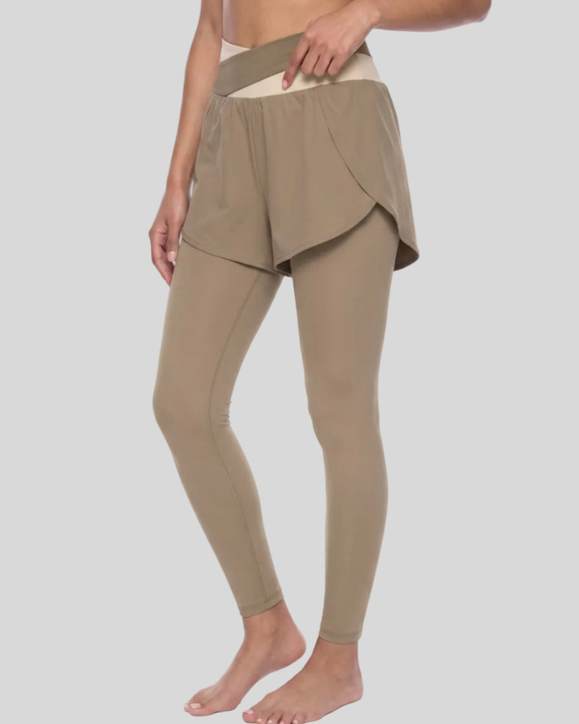 Lower body front angled view of woman wearing TrackLine Synergy Layered Leggings in light coffee with apricot crossover waistband