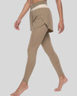Lower body left angled view of woman wearing TrackLine Synergy Layered Leggings in light coffee with apricot crossover waistband