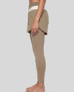 Lower body left side view of woman wearing TrackLine Synergy Layered Leggings in light coffee with apricot crossover waistband