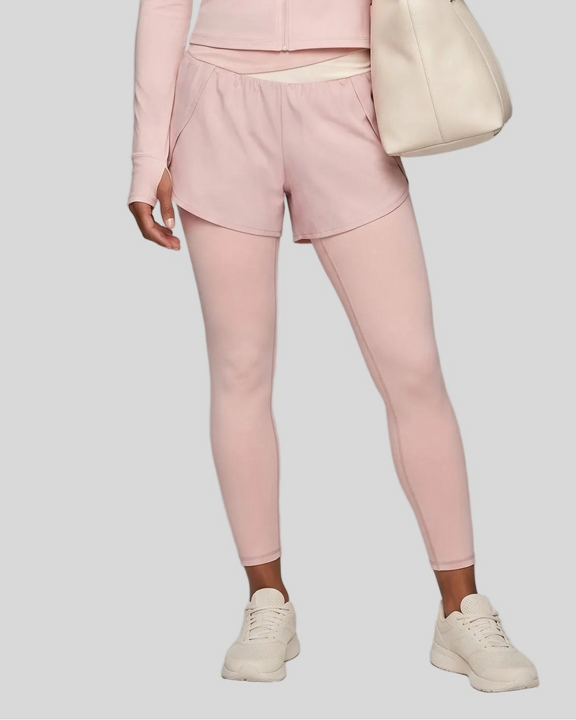 Lower body front view of woman wearing TrackLine Synergy Layered Leggings in light pink with apricot crossover waistband