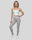 Woman wearing TrackLine Synergy Leggings in Light Gray with Light Blue crossover waistband, full body front view