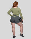 Full body back view of woman wearing TrackLine Synergy Long Sleeve Top in bean green