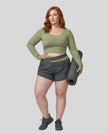 Full body view of woman wearing TrackLine Synergy Long Sleeve Top in bean green with dark gray color-block detail