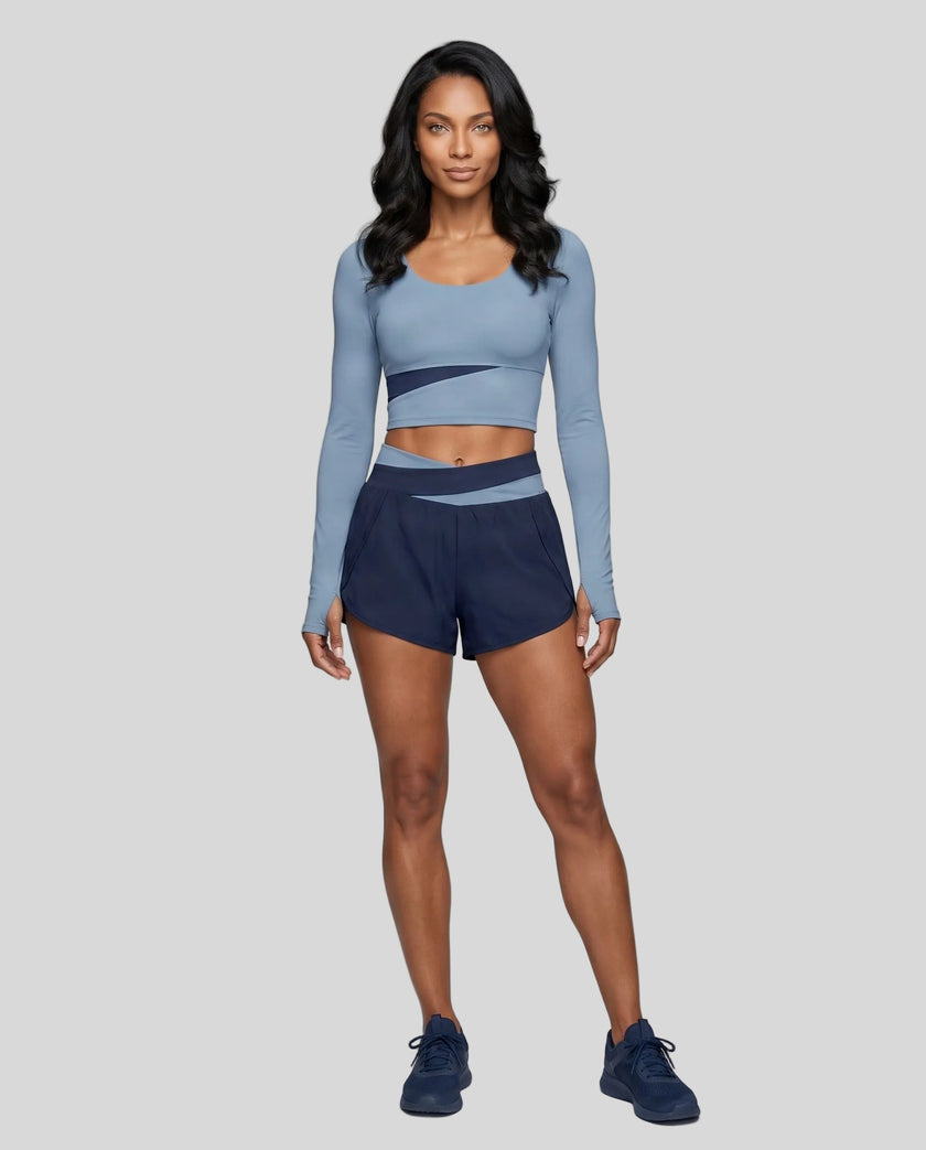 Full body view of woman wearing TrackLine Synergy Long Sleeve Top in gray blue with navy blue color-block detail