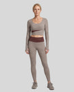 Full body view of woman wearing TrackLine Synergy Long Sleeve Top in gray purple with brick red color-block detail