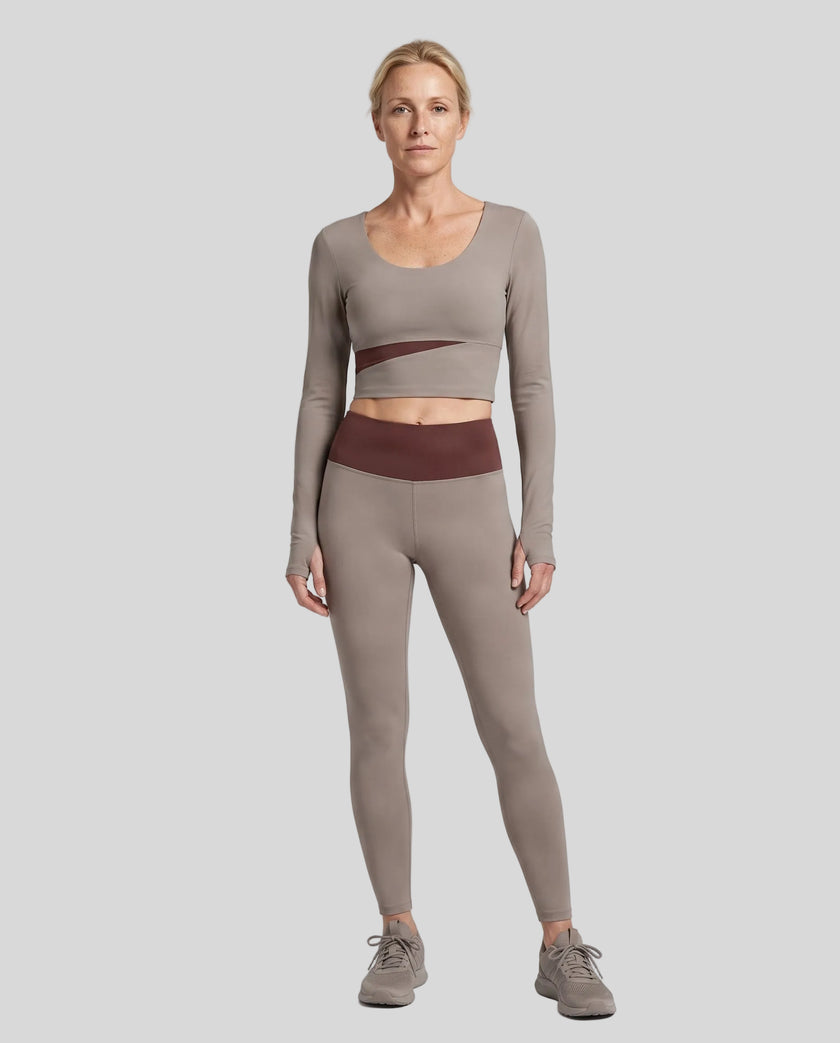 Full body view of woman wearing TrackLine Synergy Long Sleeve Top in gray purple with brick red color-block detail